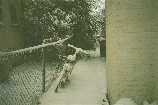 ein Fahrrad zwischen Maschendrahtzaun und Hauswand im Schnee